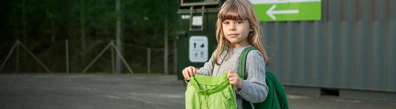 Flicka med gröna byxor framför återvinningsstationen
