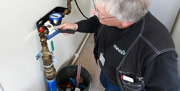 En man kontrollerar en digital vattenmätare som sitter i en konsol på väggen