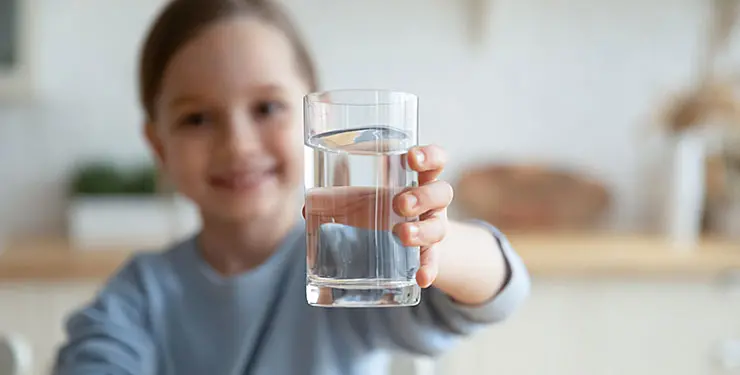 Flicka med uppsatt hår håller fram ett fyllt vattenglas