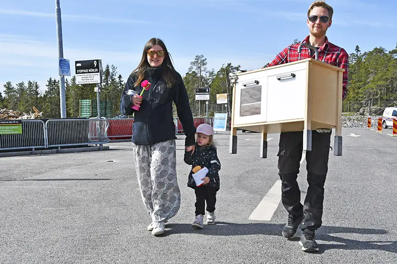 En familj med mamma, pappa och ett barn bär var sitt loppisfynd med återvinningscentralen i bakgrunden.